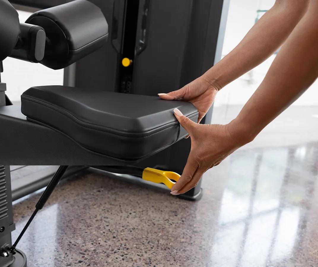 Close-up of a person adjusting the seat height on the Vision Fitness Lat Pulldown machine in Matte Black using the yellow lever below the seat.