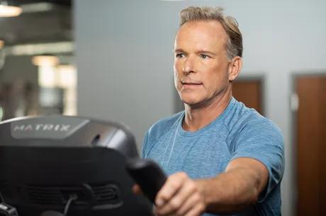 A person in a blue gray workout shirt on an elliptical