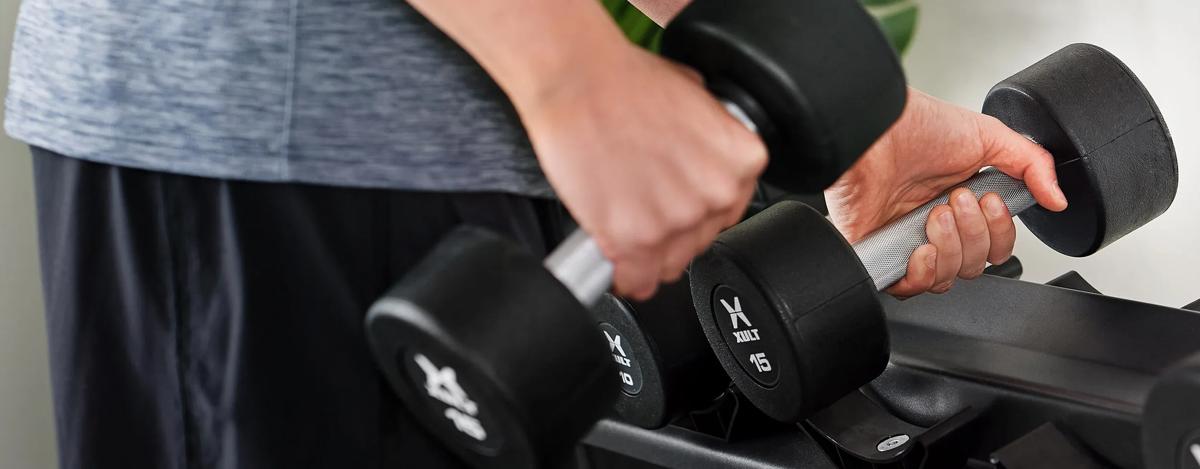 Person in workout clothes taking a pair of dumbbels from a Matte Black free weight Dumbbell Rack.