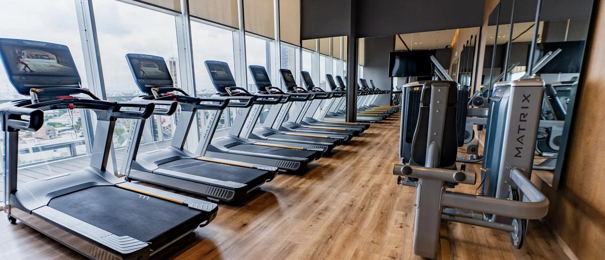 Matzwarte Matrix Fitness Onyx-cardio- en krachtapparatuur vult een modern fitnesscentrum met geïntegreerde schermen, blauwe accentverlichting, spiegelwanden en een ruim, hoogwaardig ontwerp.