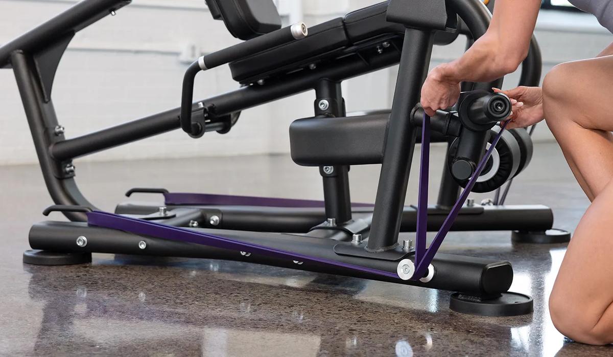 A person placing a purple resistant band on the pegs at the bottom of the machine.
