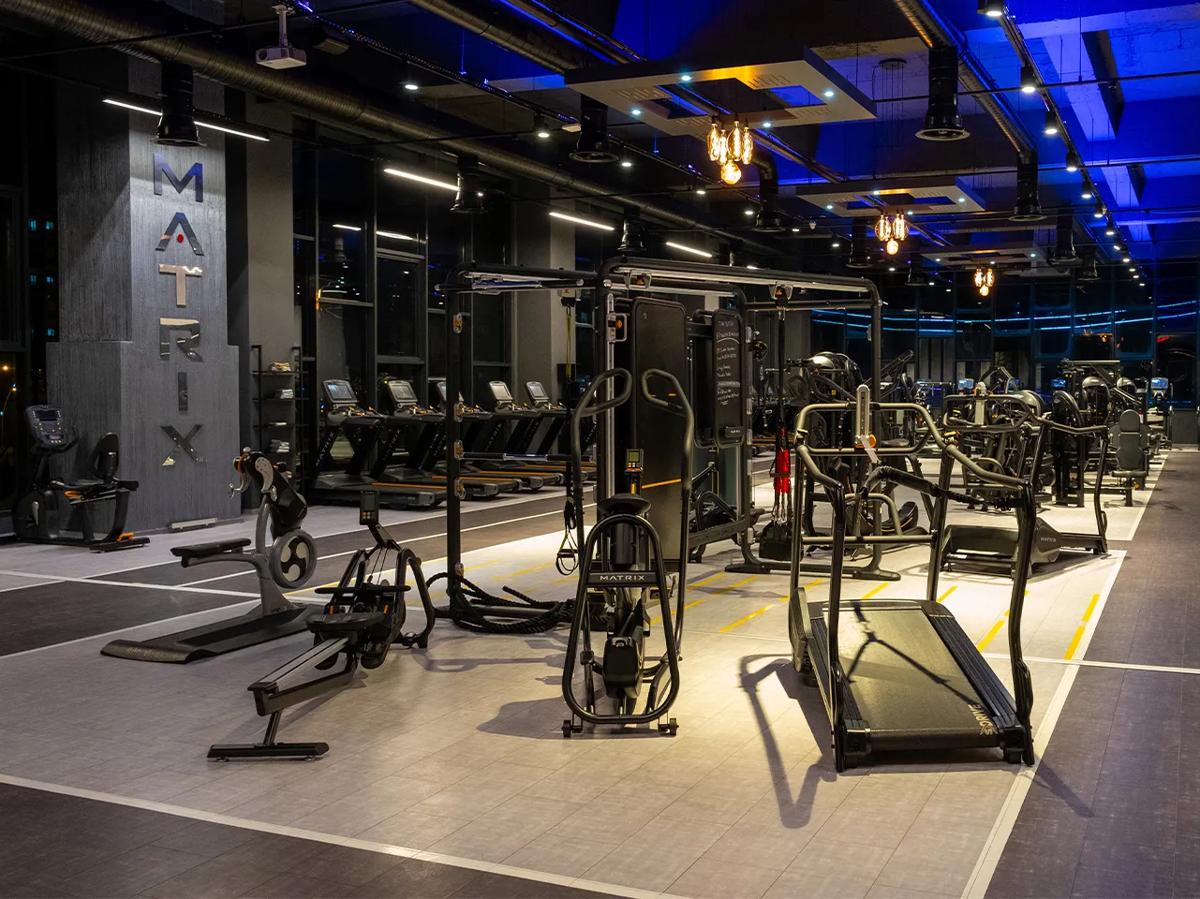 Salle de sport faiblement éclairée, décorée dans les couleurs de Matrix, présentant des appareils de musculation et de cardio dans un cadre élégant et haut de gamme.