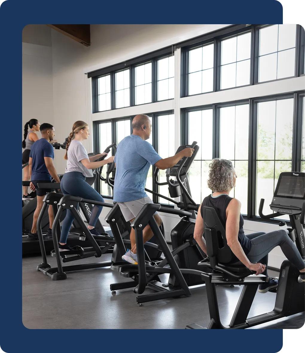 A group of people working out on Vision cardio equipment in a bright room with large windows.