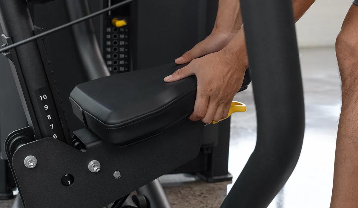 Close-up of a person adjusting the seat height on the Vision Fitness Chest Press machine in Matte Black using the yellow lever beneath the padded seat.