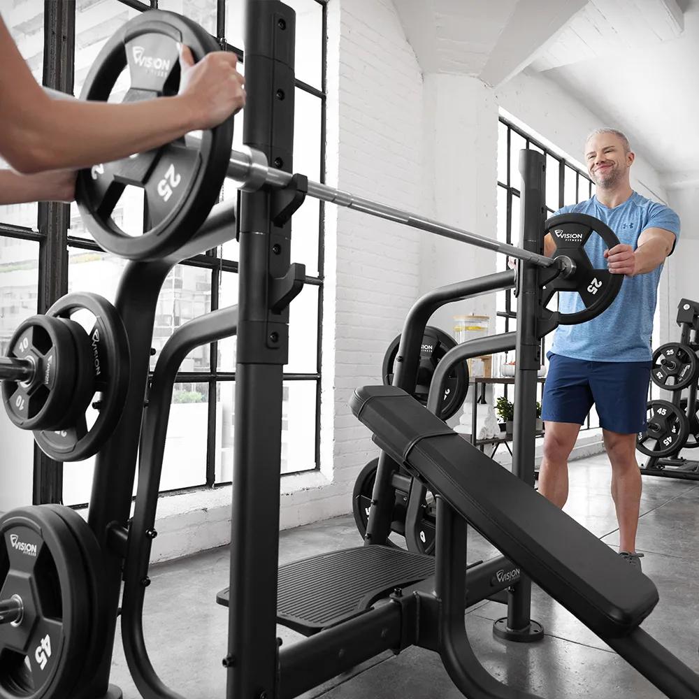 Two people on each end of the barbell loading weights in a bright room with large windows.