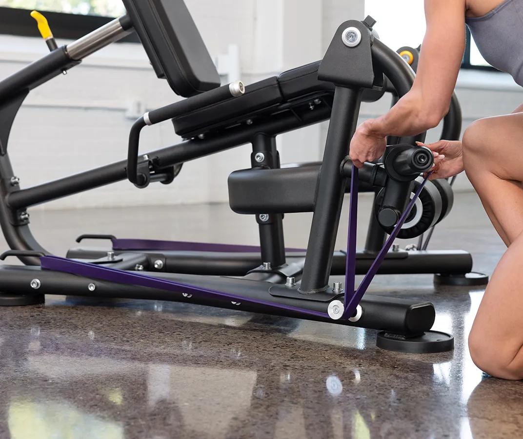 A person placing a purple resistant band on the pegs at the bottom of the machine.