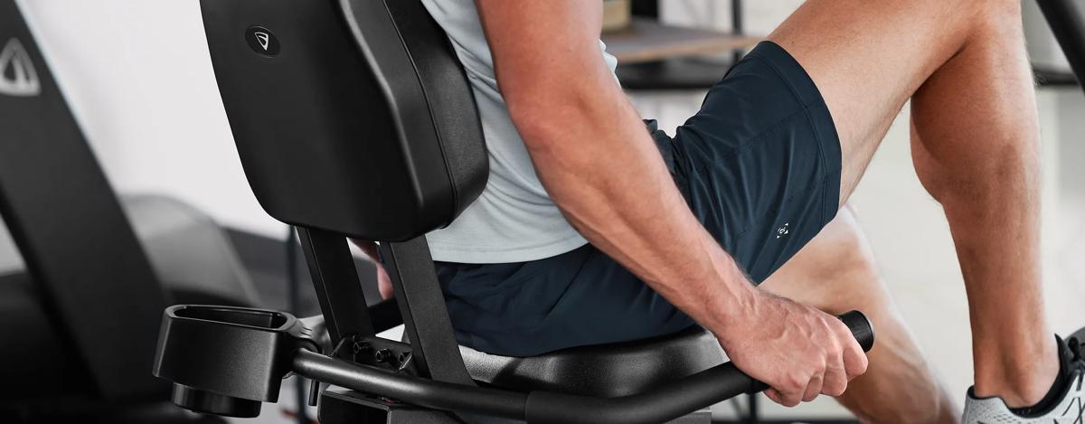 A close-up of a person's legs using the Vision Fitness Recumbent Bike, gripping the side handles for stability.
