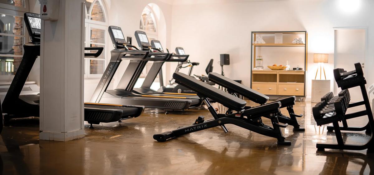 Matrix Fitness-loopbanden, verstelbare banken en dumbbells opgesteld in een lichte, moderne fitnessruimte met gepolijste vloeren, boogramen en wellnessvoorzieningen op de achtergrond.