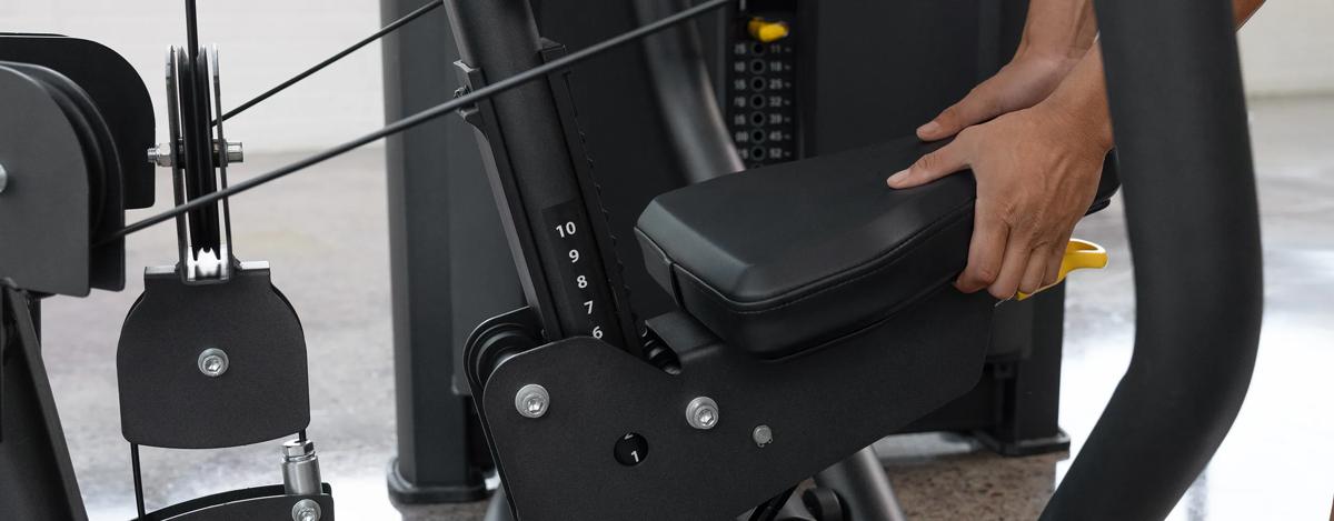 Close-up of a person adjusting the seat height on the Vision Fitness Chest Press machine in Matte Black using the yellow lever beneath the padded seat.