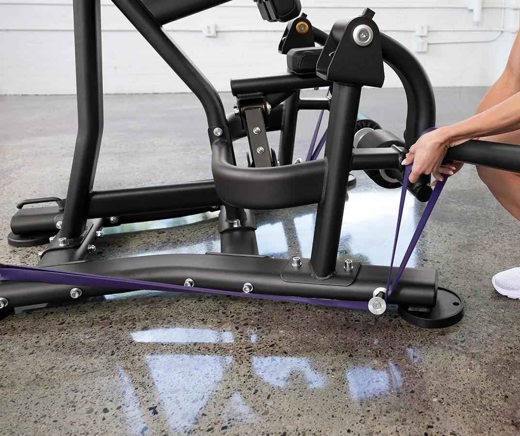 A person attaching a purple resistant band to the pegs at the bottom of the machine.