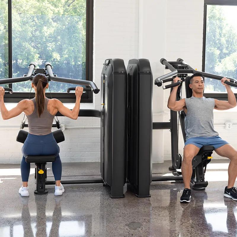 Person seated on the Vision Fitness Diverging Lat Pulldown machine in Matte Black, grasping overhead handles in preparation to begin the exercise in a well-lit gym.