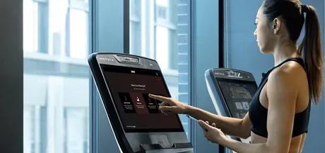 A person on a treadmill in a black top about to touch the screen to start a workout