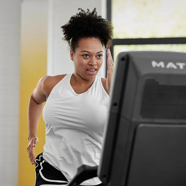 A woman in a white tank top walking on a Matrix treadmill.