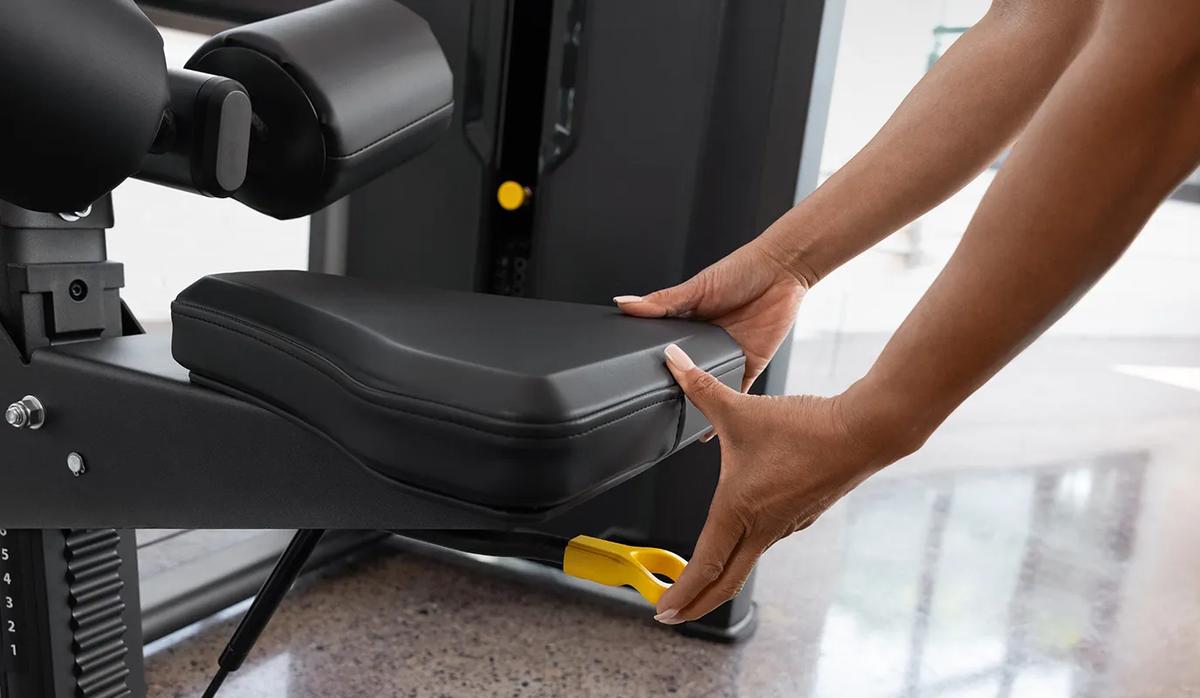 Close-up of a person adjusting the seat height on the Vision Fitness Lat Pulldown machine in Matte Black using the yellow lever below the seat.