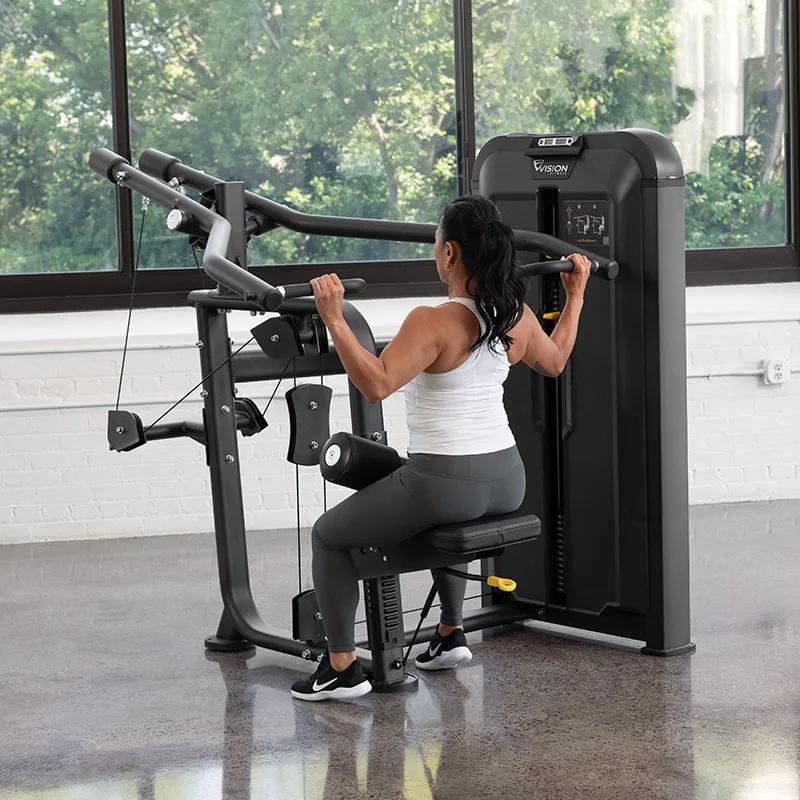 Person performing a lat pulldown on the Vision Fitness Lat Pulldown machine in Matte Black, seated in a bright gym with arms bent and handles pulled to shoulder height.