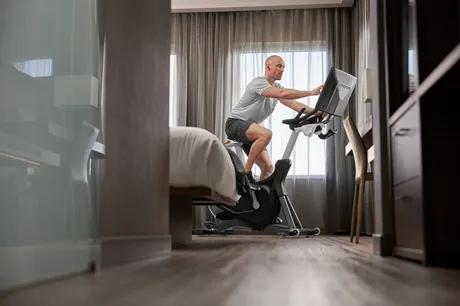 En person på et hotelværelse sidder på en træningscykel og rører skærmen