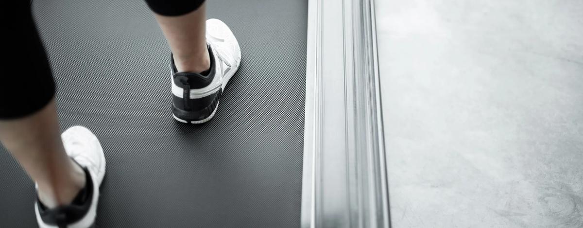 Close-up of a person’s feet in white athletic shoes walking on a treadmill.