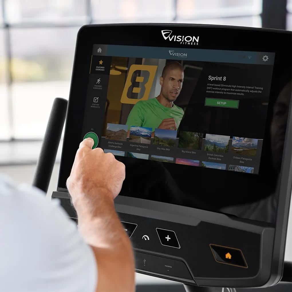 Two people exercising on Vision Fitness stationary bikes with interactive screens in a bright, modern gym.