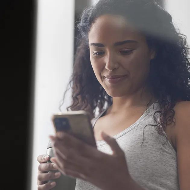 En kvinde kigger på sin telefon og smiler.
