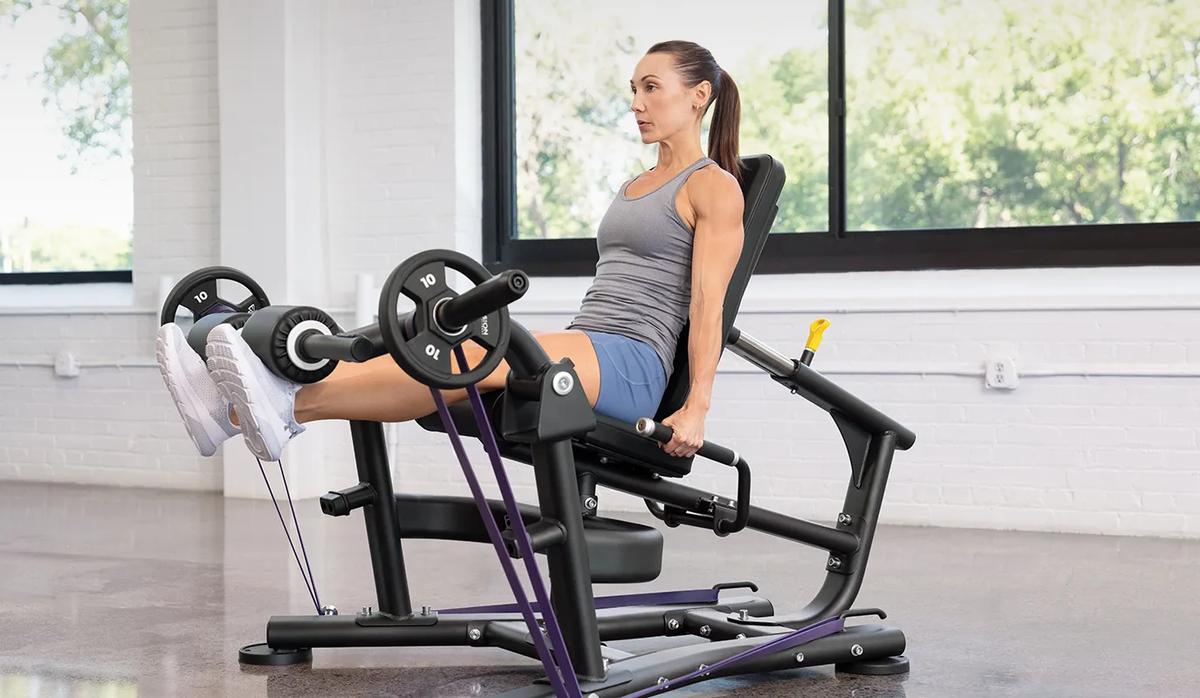 A person with their legs straight out with weights and resistant bands on the Vision Leg Extension.