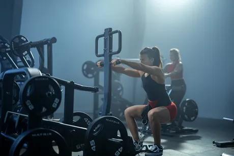 A person in workout clothes in a dark gym mid squat using the belt attachment