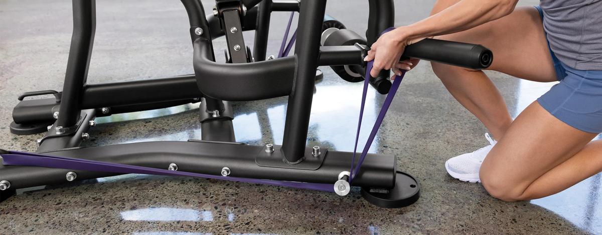 A person attaching a purple resistant band to the pegs at the bottom of the machine.