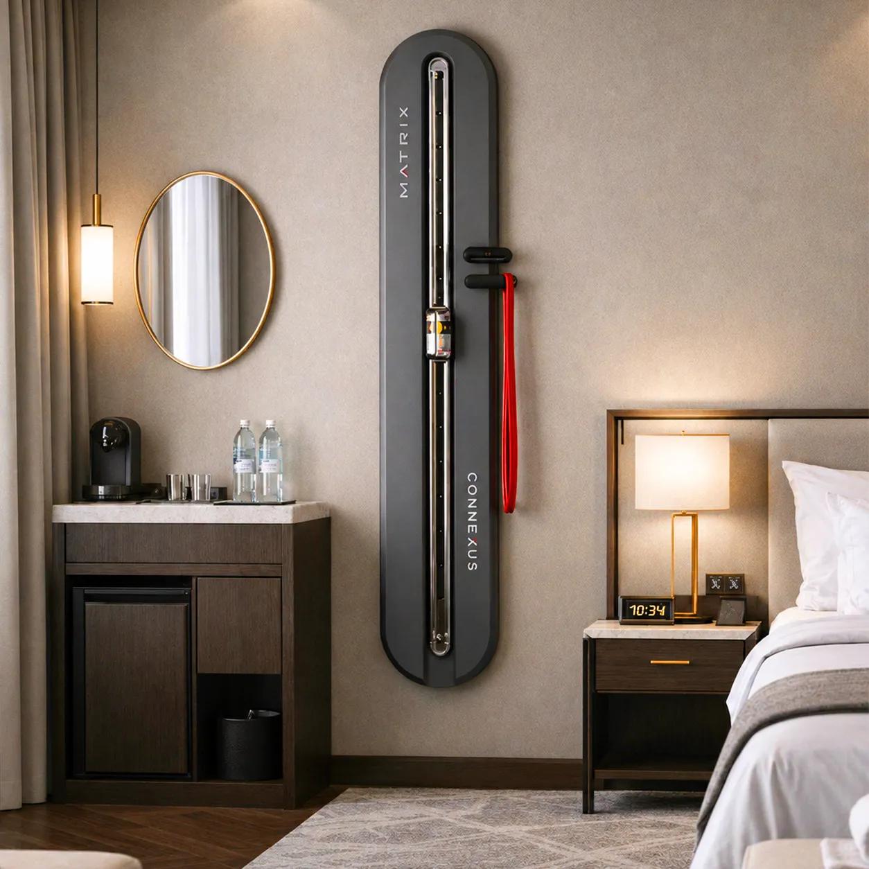 Matzwarte aan de muur gemonteerde Matrix Fitness Connexus-trainer geïnstalleerd in een hotelkamer, die een compacte fitnessoplossing voor op de kamer biedt met weerstandsbanden.