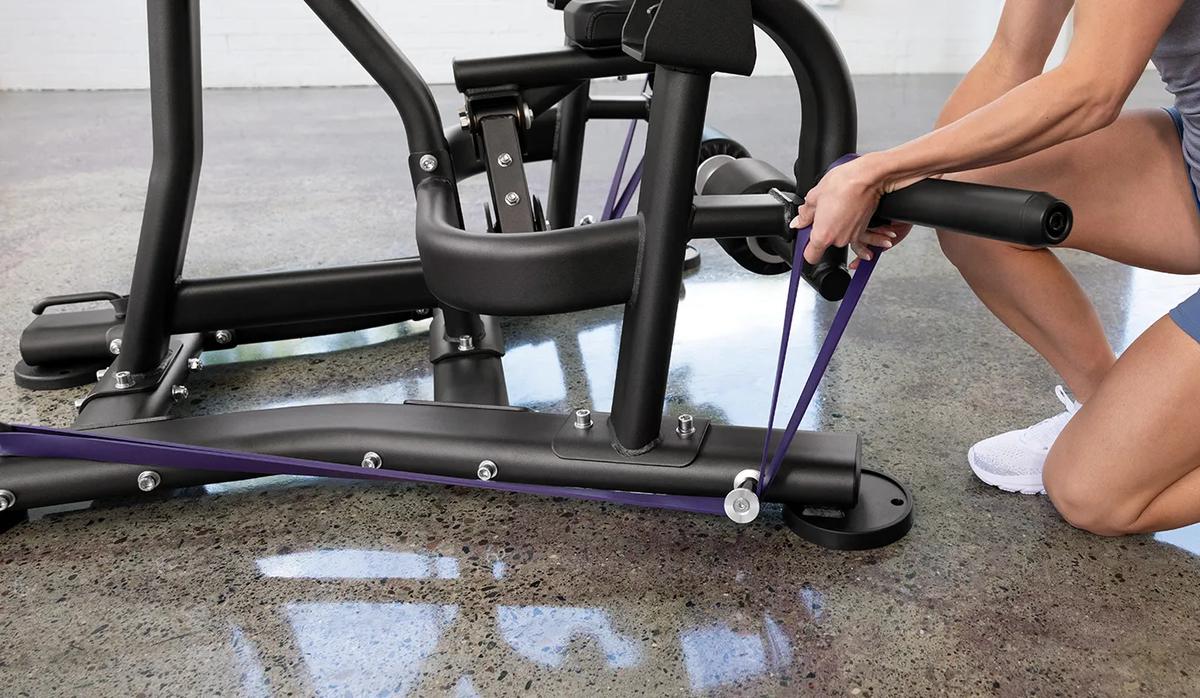 A person attaching a purple resistant band to the pegs at the bottom of the machine.