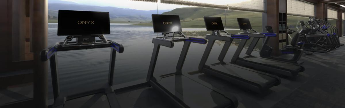 Matrix Fitness Onyx-loopbanden in Matte Black staan in een luxe fitnessruimte met uitzicht op een meer en glooiende heuvels. Grote geïntegreerde displays en blauwe accentverlichting zorgen voor een premium trainingsomgeving.