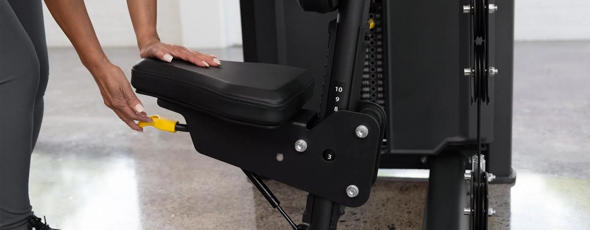 Close-up of a person adjusting the seat height on the Vision Fitness Shoulder Press machine in Matte Black using the yellow lever beneath the seat.