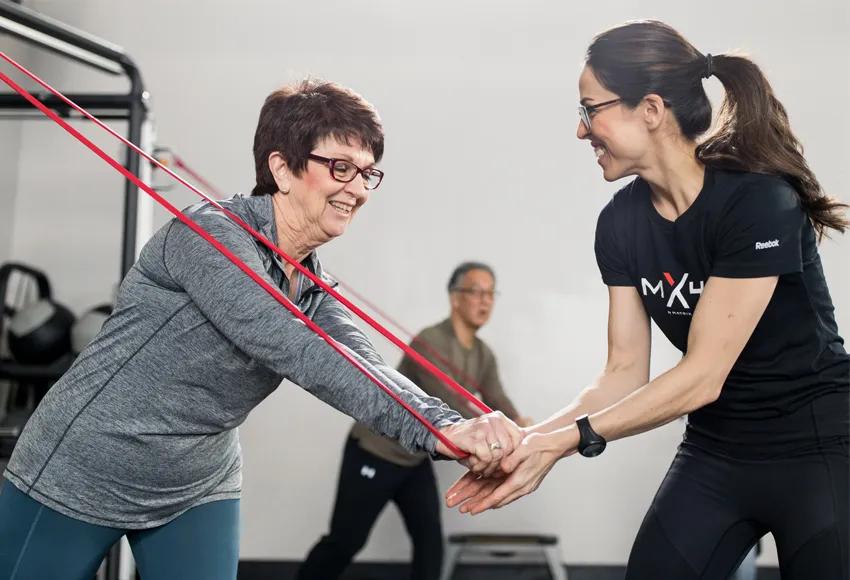 A person using a red band with another person in a black mx4 t-shirt training them