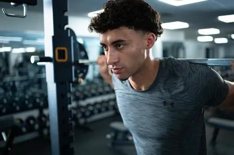 A person in a gray tee shirt with a barbell on their back about to do a squat