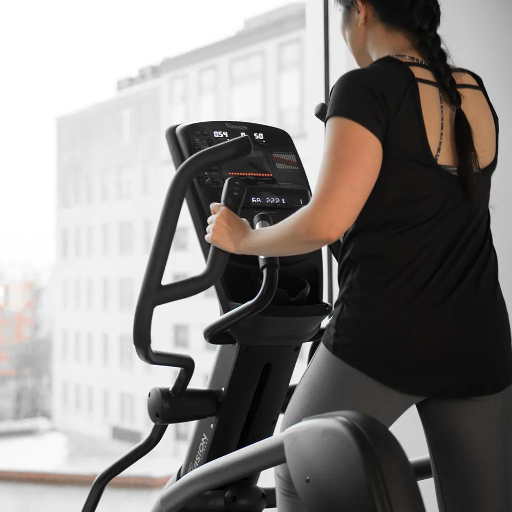 A person exercises on a Vision Fitness elliptical in a bright gym with large windows.
