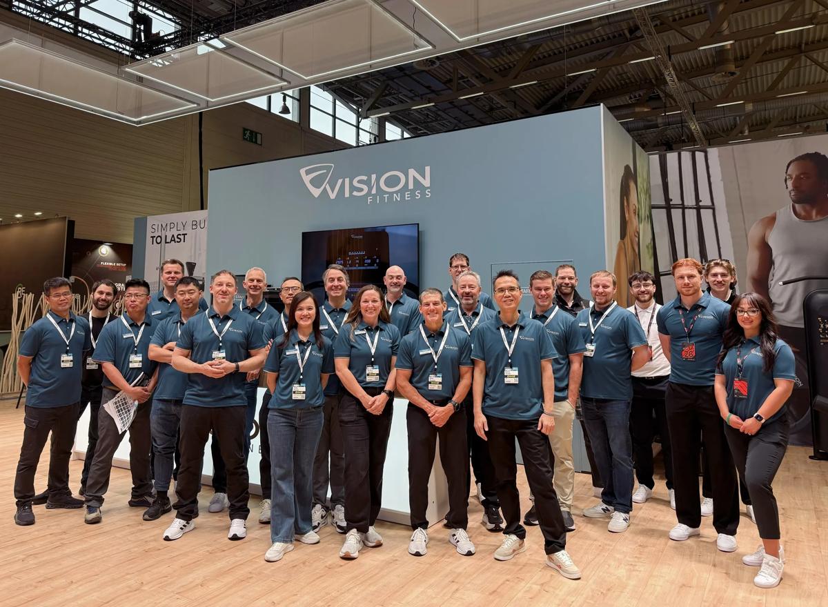 A group of Vision Fitness employees standing together smiling in a trade show booth.