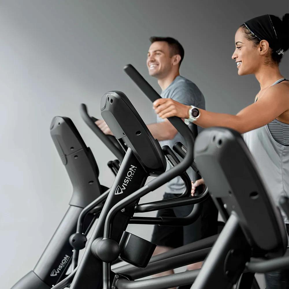 兩個人在使用 Vision Fitness 橢圓機時面帶微笑。