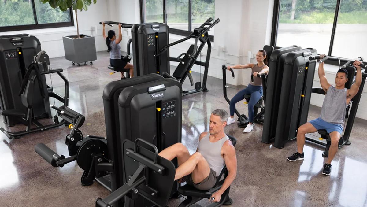 A group of people working out on the new line of Vision Fitness Keystone Selectorized Series in a bright gym.