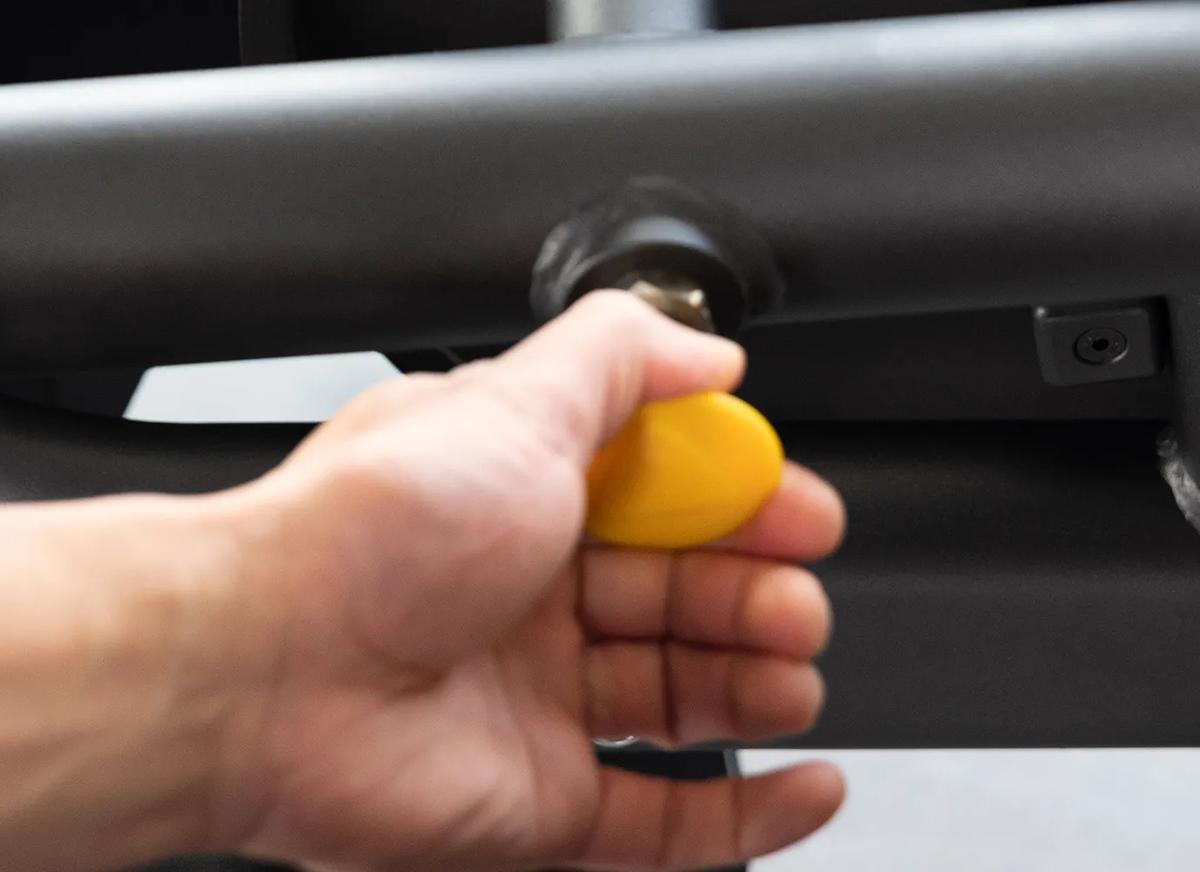 Close-up of a person using the Keystone Seated Leg Curl adjustment arm with yellow pop-pins.