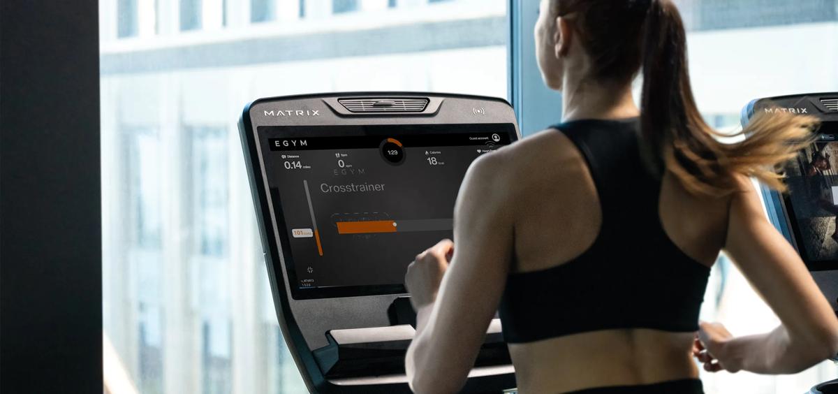 Una persona con un top sportivo nero corre su un tapis roulant Matrix utilizzando il sistema EGYM.