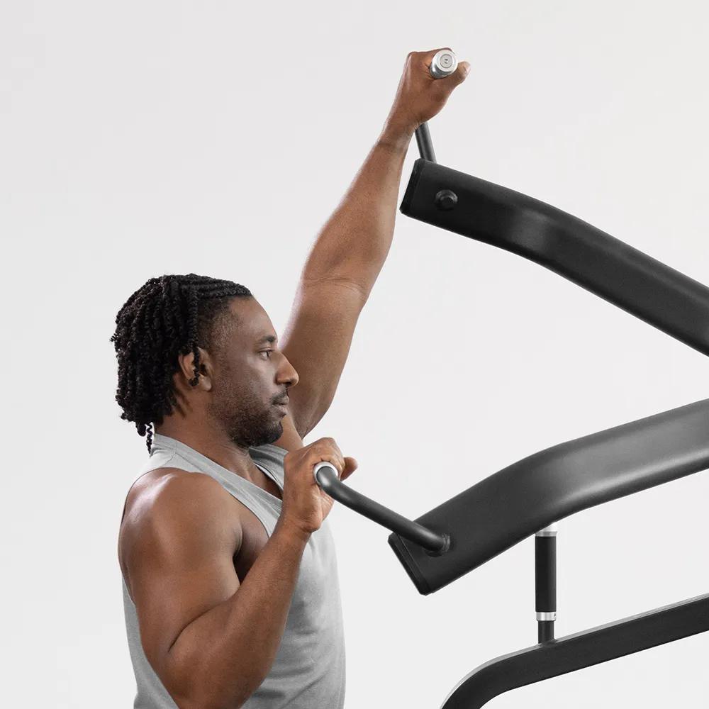 A person in a gray workout tank using shoulder press with left arm fully extended.
