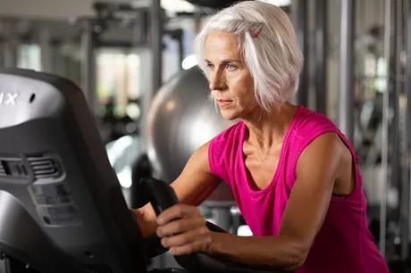 A person in a pink workout tank on upright cycle in a gym