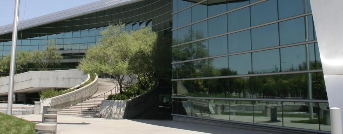 Sunny exterior view of a municipal facility with large windows, decorative trees and a staircase leading to the entrance.