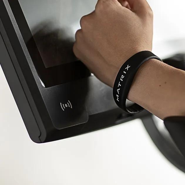 En person trykker sit Matrix smart-armbånd mod en Matrix Fitness-konsol.
