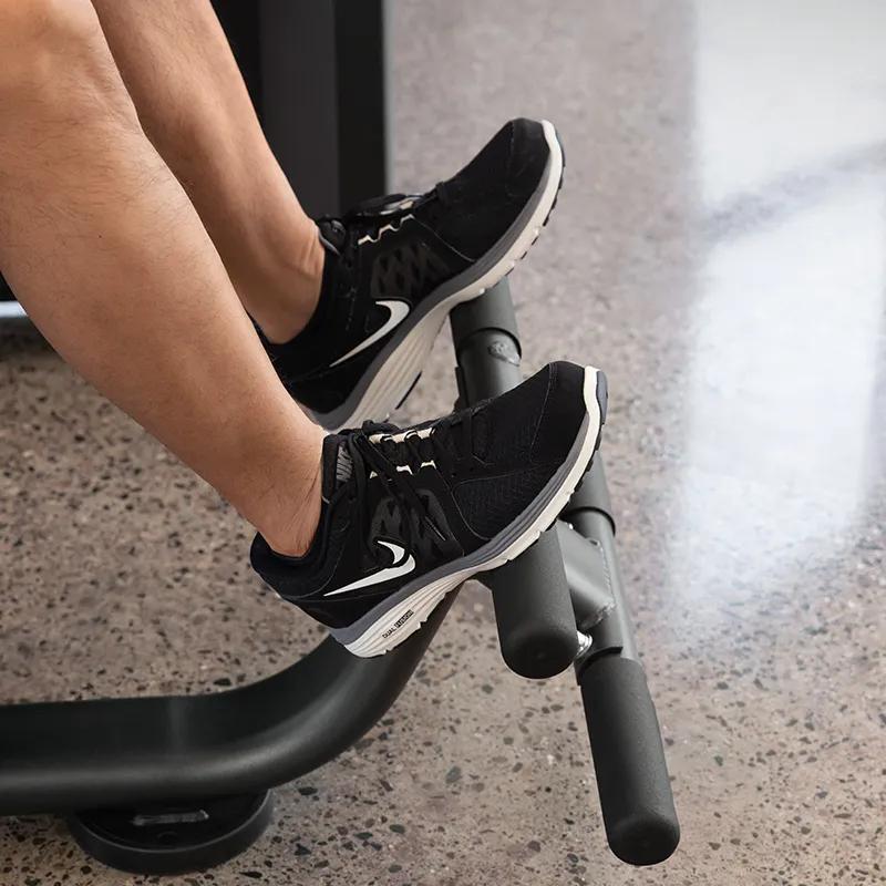 Close-up of a user's feet secured under padded rollers on the Vision Fitness Back Extension machine, showing proper foot placement for stability during the exercise.