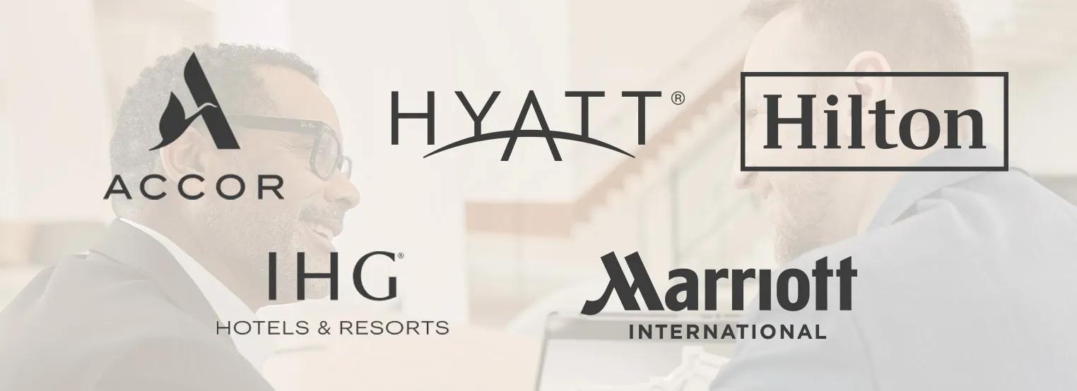 Logo's van Accor, Hyatt, Hilton, IHG Hotels & Resorts en Marriott weergegeven over een onscherpe achtergrond van twee vergaderende professionals, die grote hospitalitymerken vertegenwoordigen.