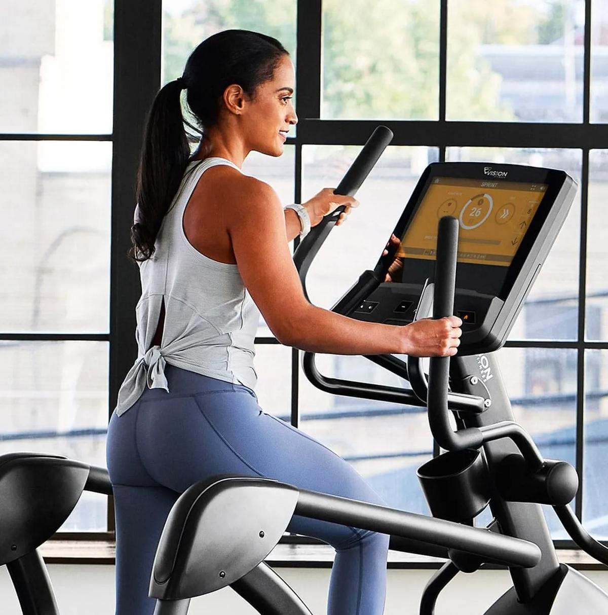 A person in blue workout leggings on an Vision elliptical doing a Sprint 8 program infront of a large window.