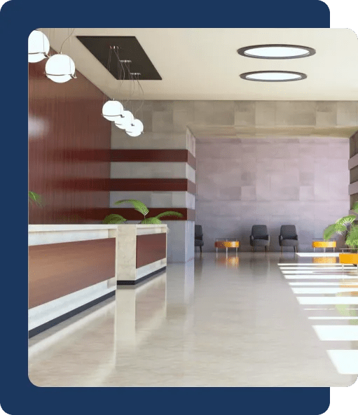 A bright office lobby with front desks, plants and some chairs on the back wall.