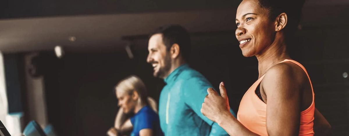 Three smiling people in workout clothes running side-by-side on Vision treadmills.