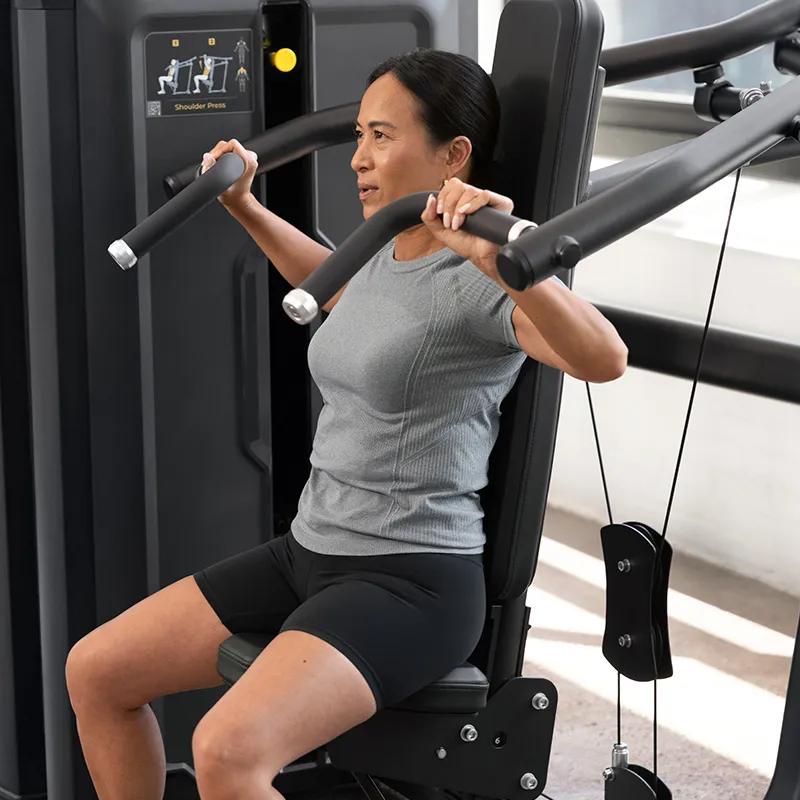 Person using the Vision Fitness Shoulder Press machine in Matte Black, seated with arms bent and hands gripping the overhead press handles in a gym setting.