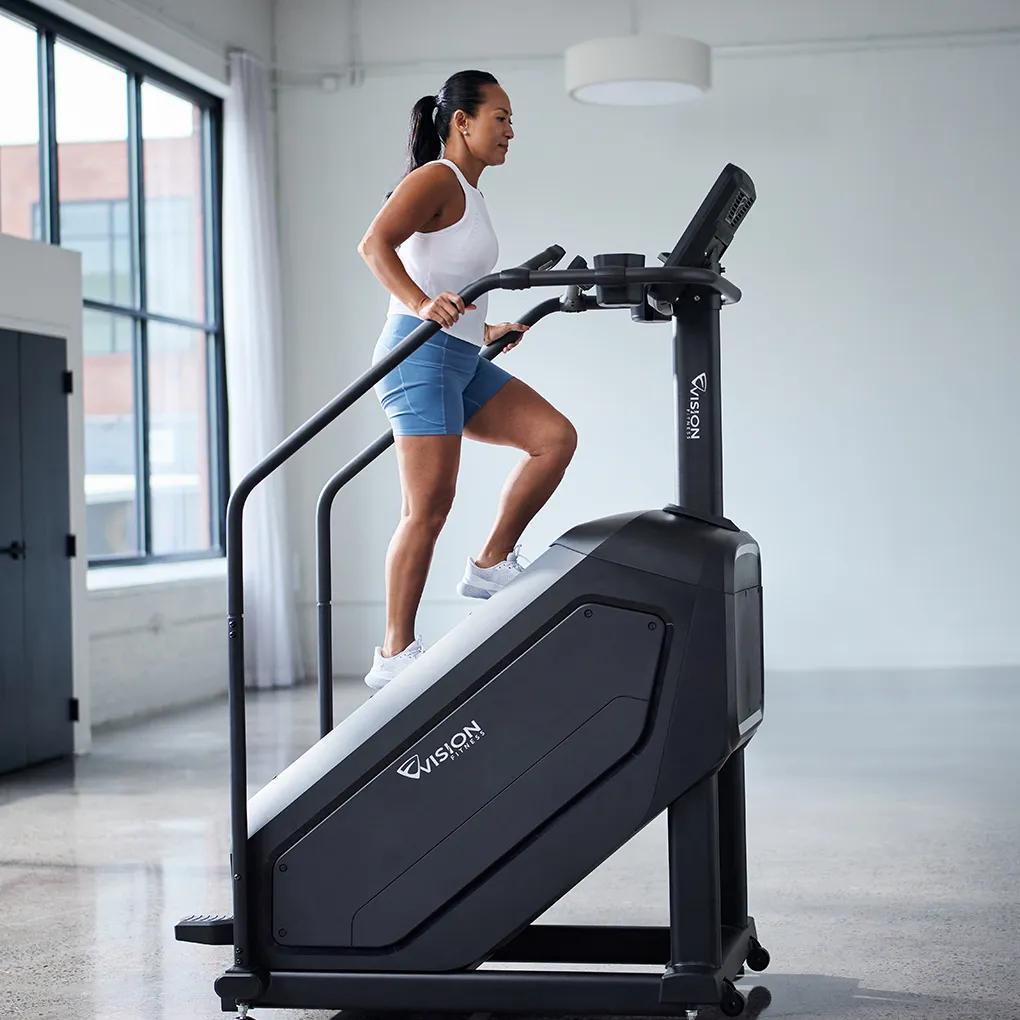 Person exercising on a Vision Fitness stair climber in a bright, modern gym.