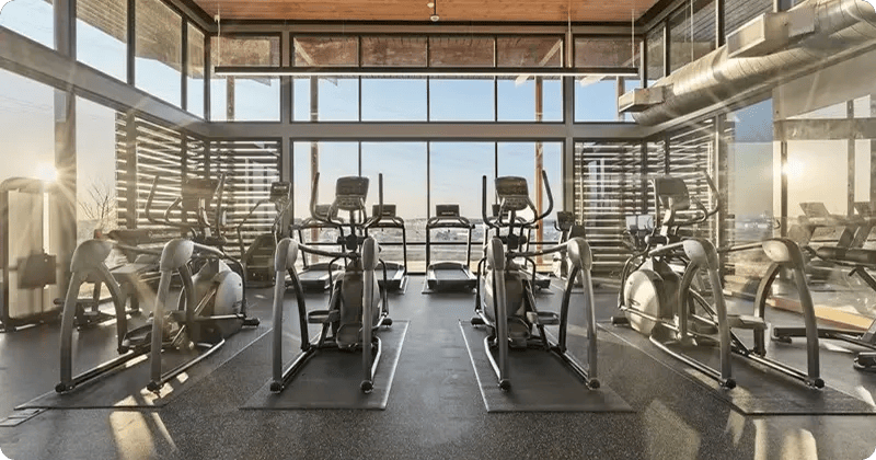 Fitness equipment in a gym with all windows and the sun rising in
